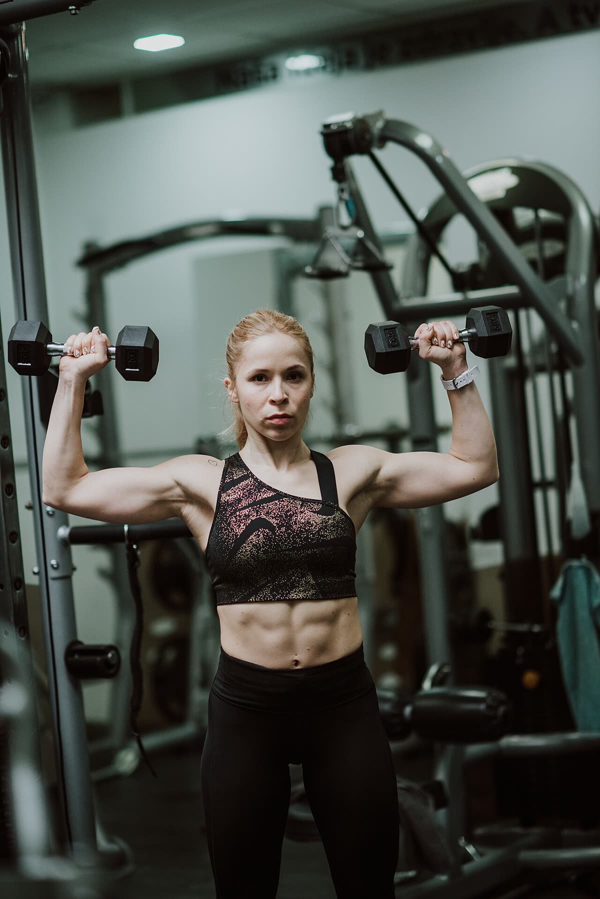 A woman doing a dumbbell shoulder press in a gym
